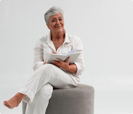 An old woman sitting on a cushion, reading a book peacefully.